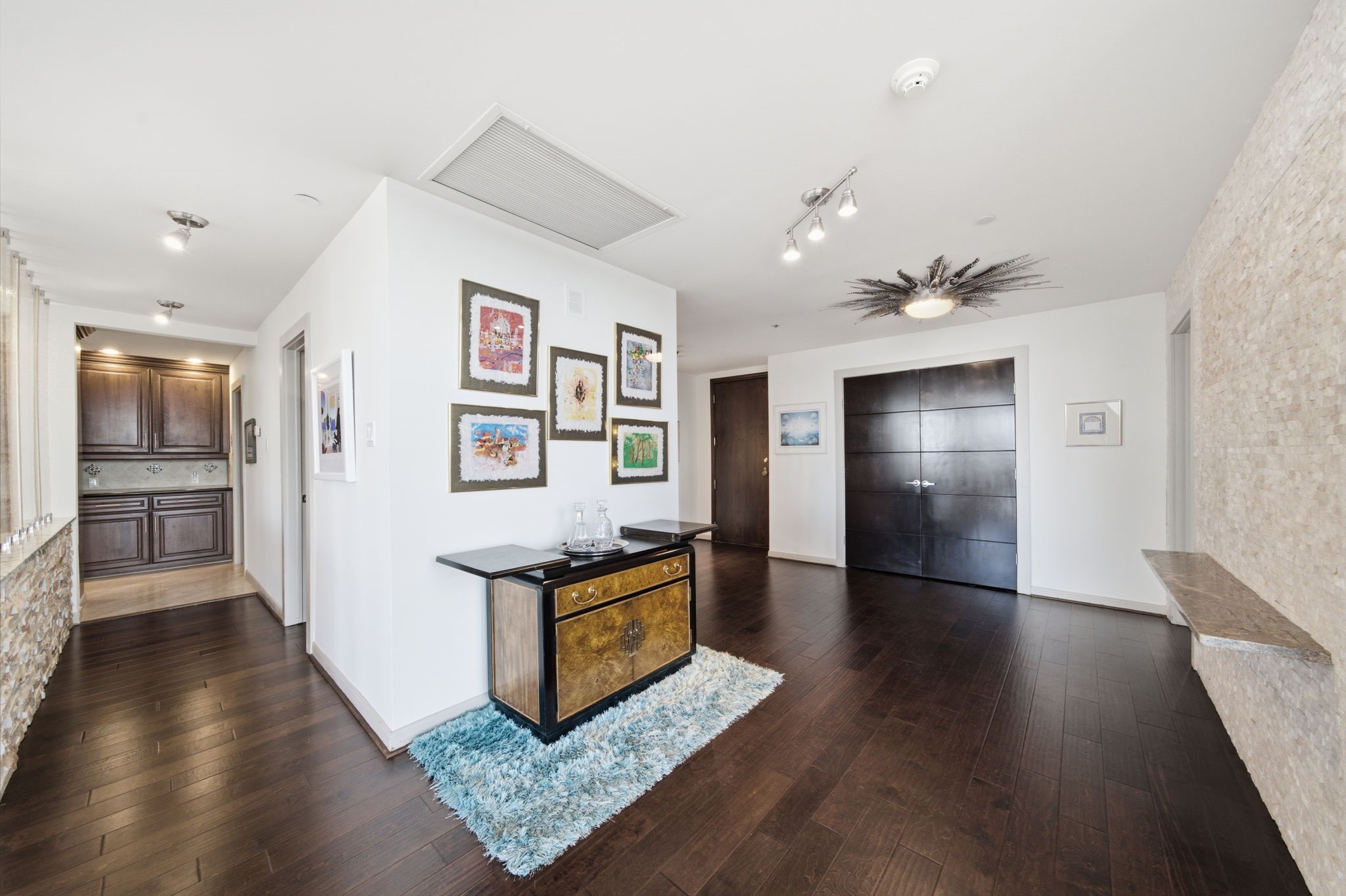 3350 McCue Road, Unit 2402 Houston, TX 77056 - Photo 9 of 49 Rich dark hardwood floors flow seamlessly through this open transition area, connecting the living spaces to the kitchen with gallery-style wall space for art. Statement designer light fixtures and a stone accent ledge complement the sophisticated, modern aesthetic throughout the residence.