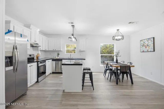 a kitchen with stainless steel appliances granite countertop a stove a refrigerator a kitchen island a dining table and chairs with wooden floor