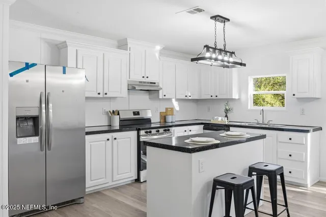 a kitchen with stainless steel appliances kitchen island a refrigerator a stove a sink and white cabinets