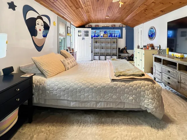 a spacious bedroom with a bed and a flat tv screen on dresser