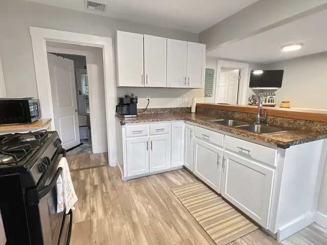 a kitchen with a sink dishwasher a stove and white cabinets with wooden floor