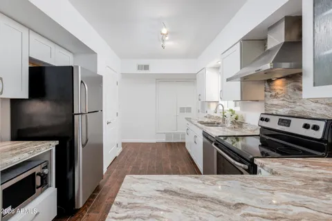 a kitchen with stainless steel appliances granite countertop a stove top oven a sink dishwasher a refrigerator and a oven with wooden floor