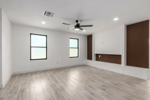 an empty room with wooden floor ceiling fan and windows