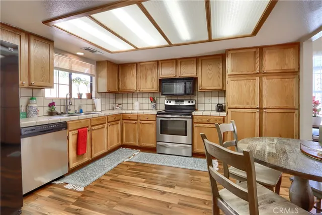 a kitchen with stainless steel appliances granite countertop a sink a stove a refrigerator cabinets a dining table and chairs