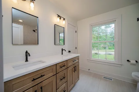 a bathroom with a toilet a sink a mirror a window and vanity