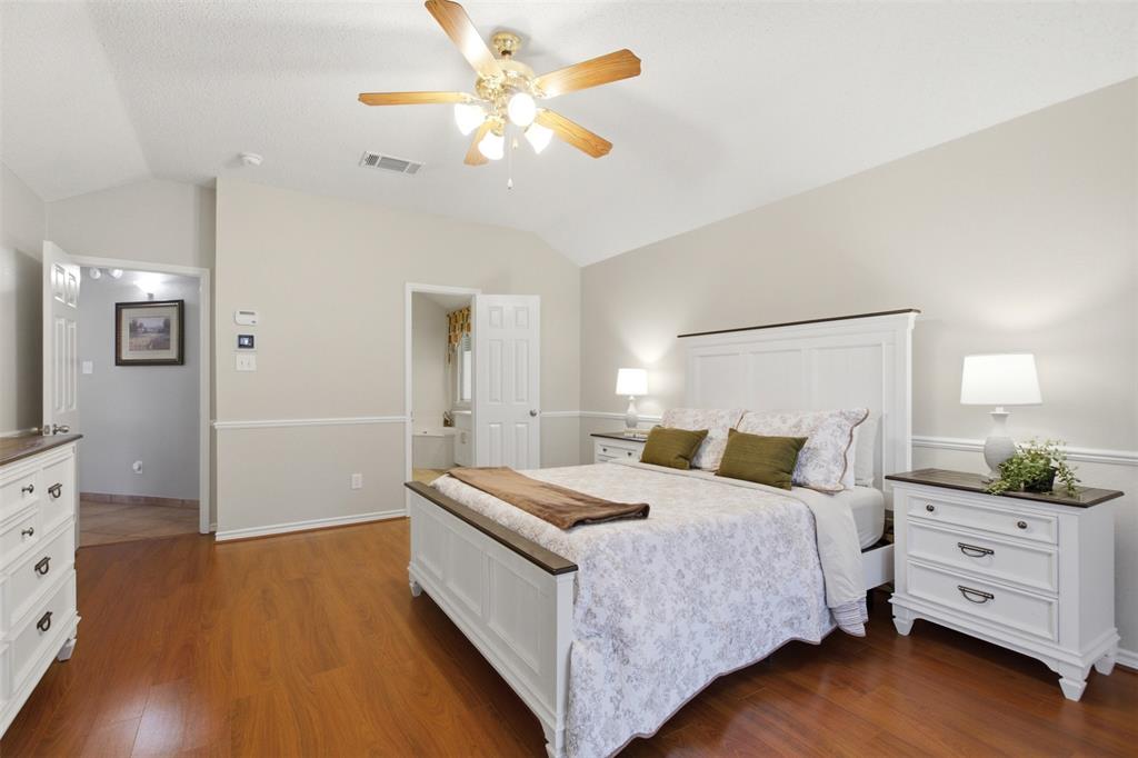 4218 Glistening Spring Rowlett, TX 75088 - Photo 18 of 39 Bedroom featuring wood-finish flooring, vaulted ceilings, a ceiling fan with light fixture, and neutral wall tones with wainscoting