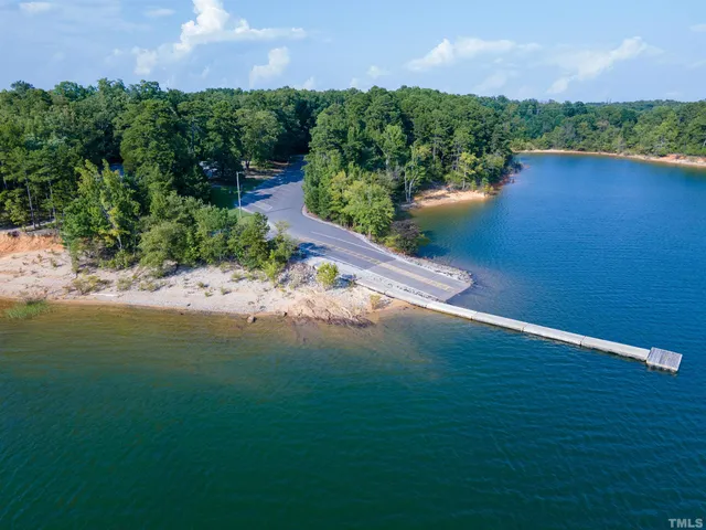 a view of a lake with lawn chairs and large trees
