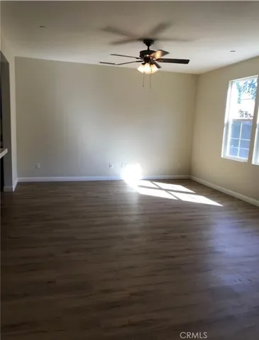 an empty room with wooden floor fan and windows