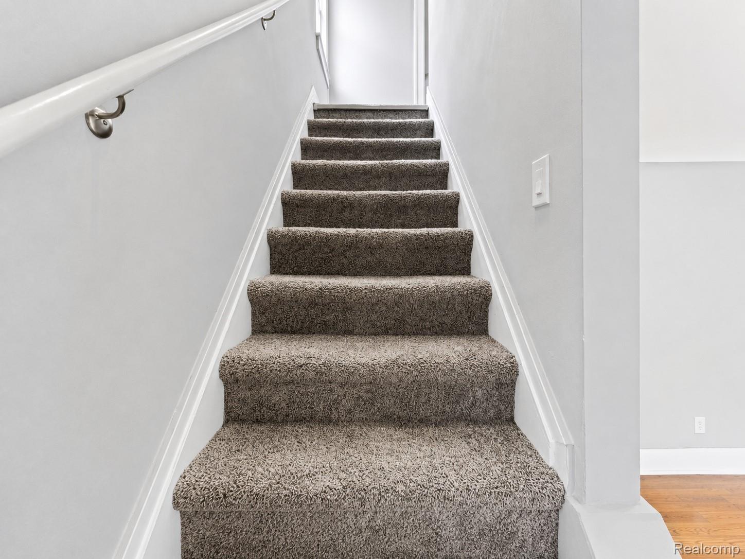 9175 Devonshire Road Detroit, MI 48224 - Photo 10 of 23 Carpeted staircase featuring a painted handrail with brushed nickel brackets and white trim detailing
