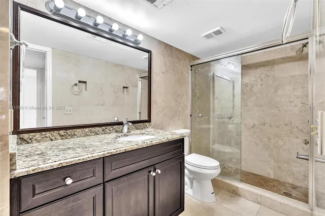 a bathroom with a granite countertop sink toilet a mirror and shower