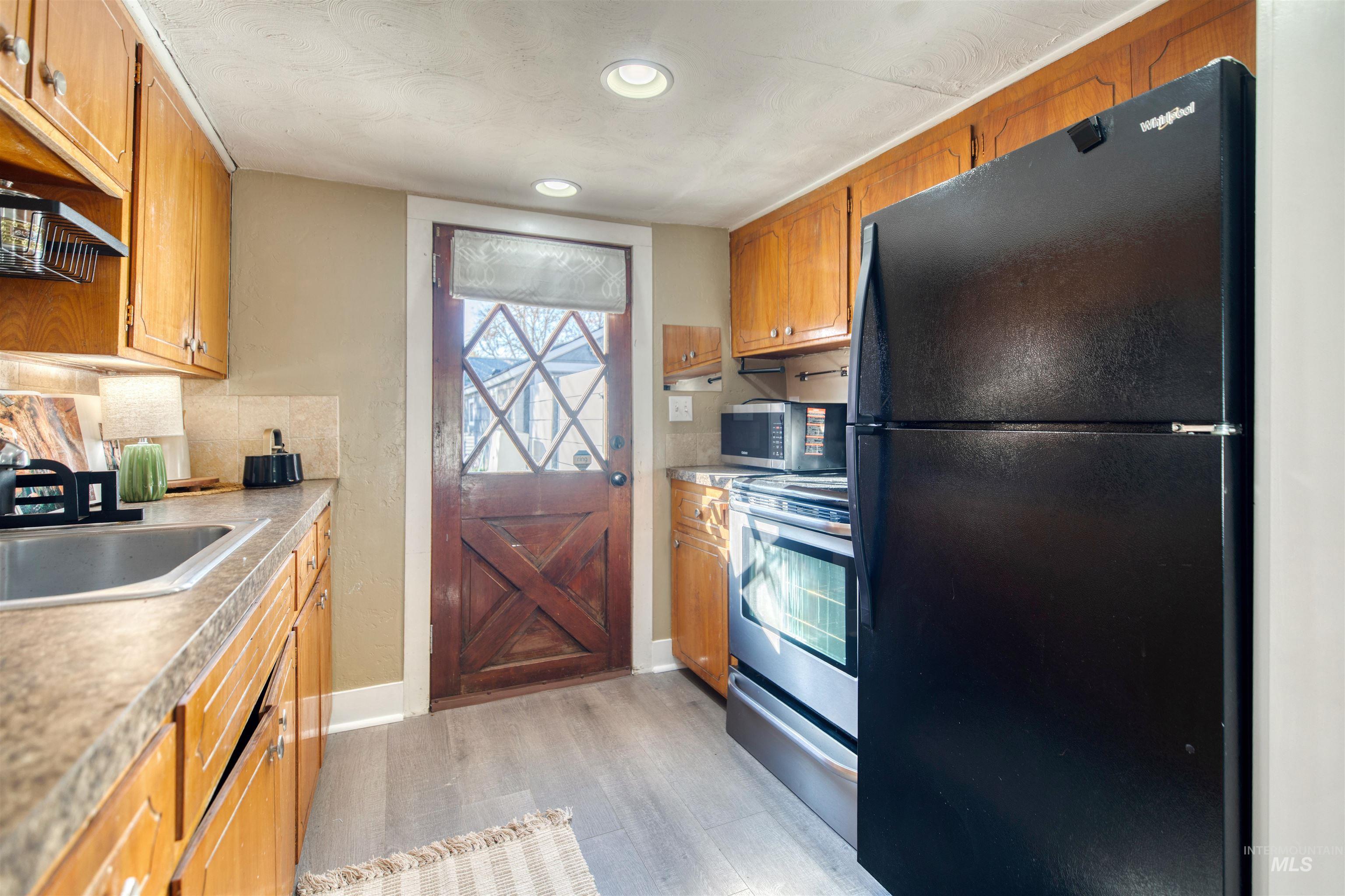 3311 West Hamilton Street Boise, ID 83705 - Photo 16 of 32 Kitchen with appliances with stainless steel finishes, light wood-style flooring, decorative backsplash, light countertops, and brown cabinets