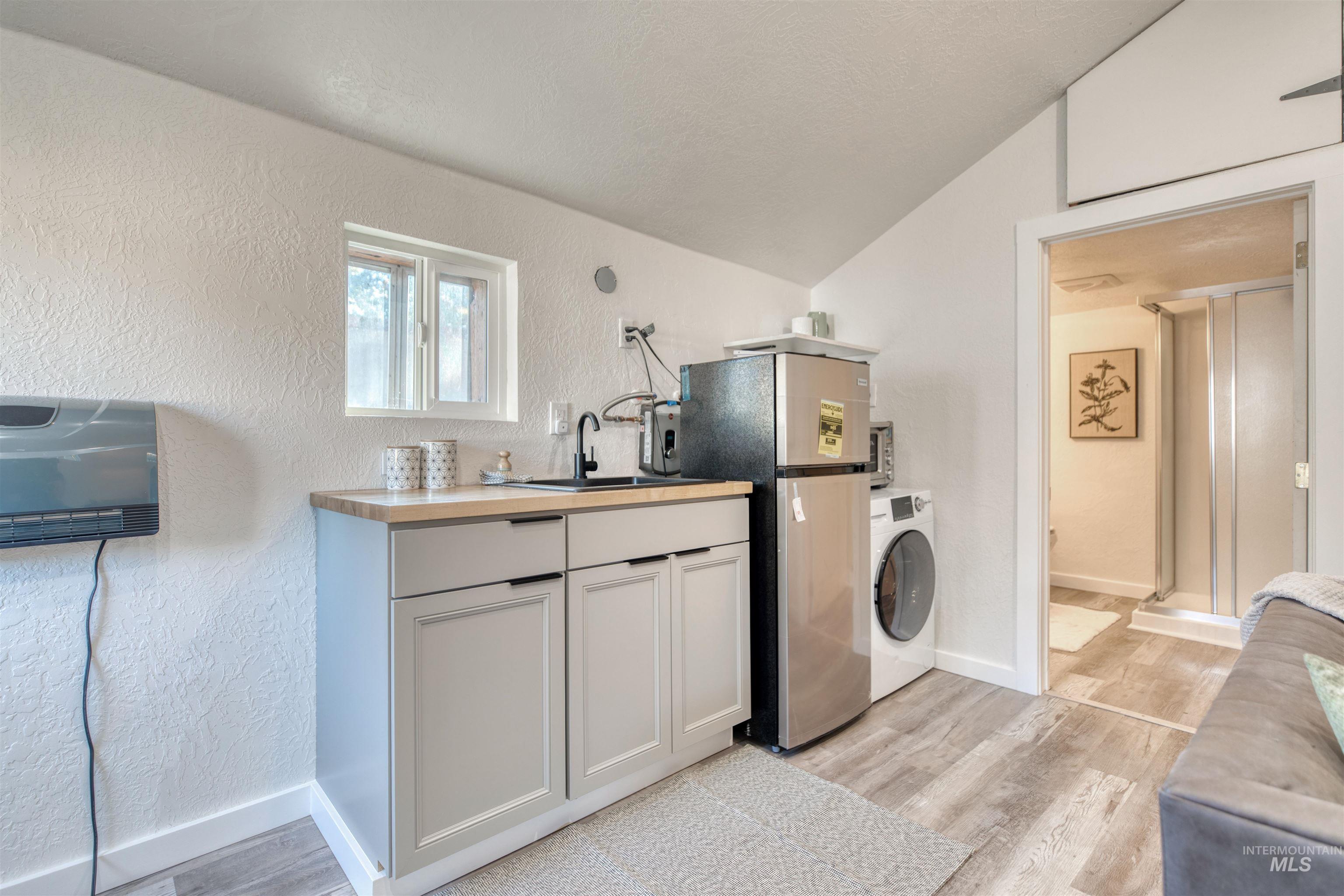 3311 West Hamilton Street Boise, ID 83705 - Photo 27 of 32 Kitchen featuring a textured wall, light wood-style flooring, freestanding refrigerator, washer / dryer, and vaulted ceiling