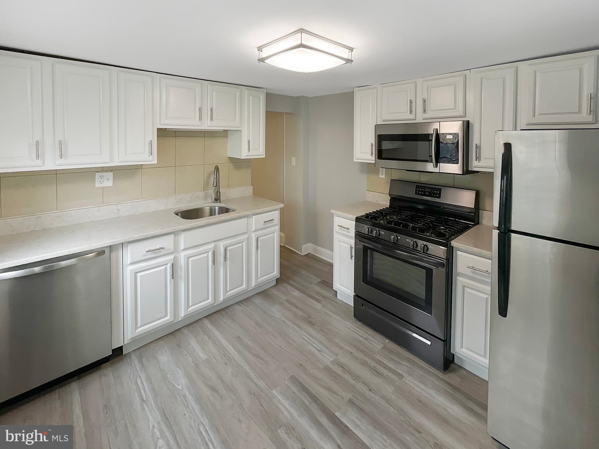 160 McClellan Street Philadelphia, PA 19148 - Photo 2 of 29 a kitchen with white cabinets stainless steel appliances and wooden floor