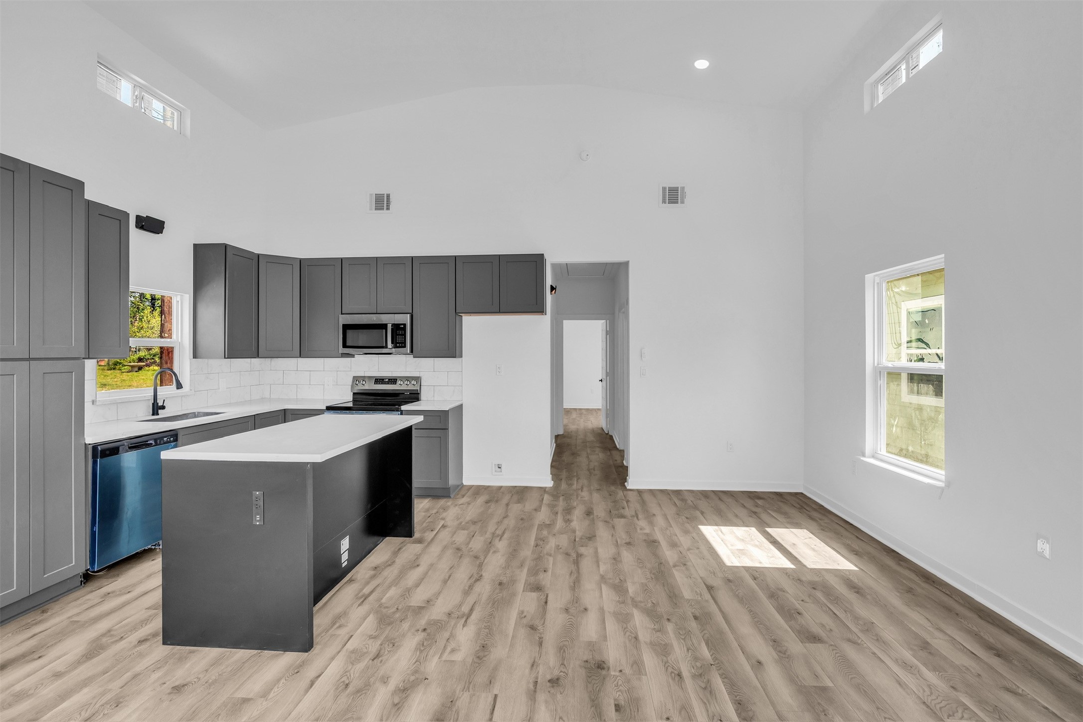 117 Rain Forest Road Onalaska, TX 77360 - Photo 20 of 30 Modern kitchen with sleek gray cabinetry, stainless steel appliances, and a spacious island, complemented by elegant wood flooring and abundant natural light.