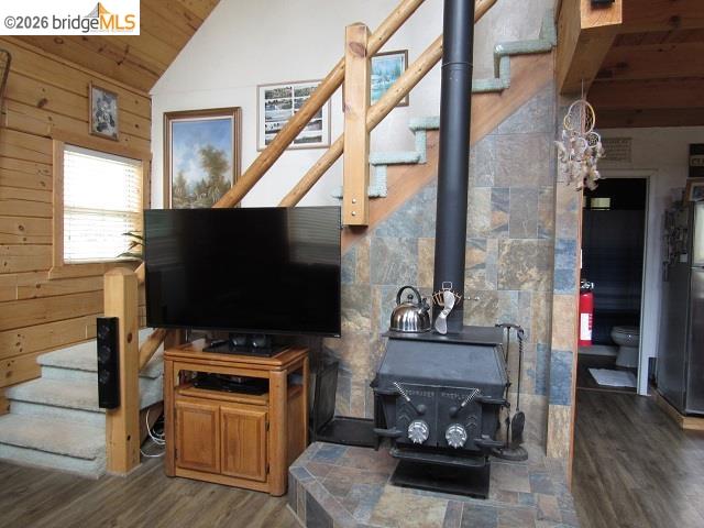 17375 Star Ridge Road Twain Harte, CA 95383 - Photo 8 of 24 Wood-paneled wall with a window, wood-finish flooring, a cast iron wood-burning stove on a tiled hearth, and a wood staircase with carpeted treads