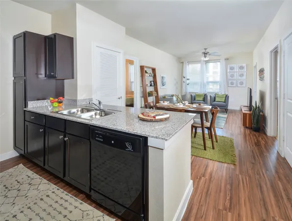a dining hall with stainless steel appliances granite countertop a refrigerator a sink dishwasher a dining table and chairs with wooden floor