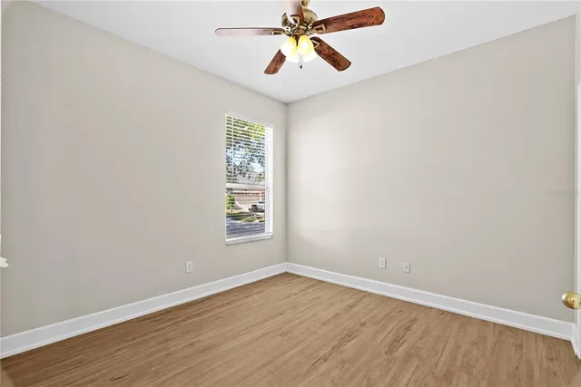 an empty room with wooden floor chandelier fan and windows