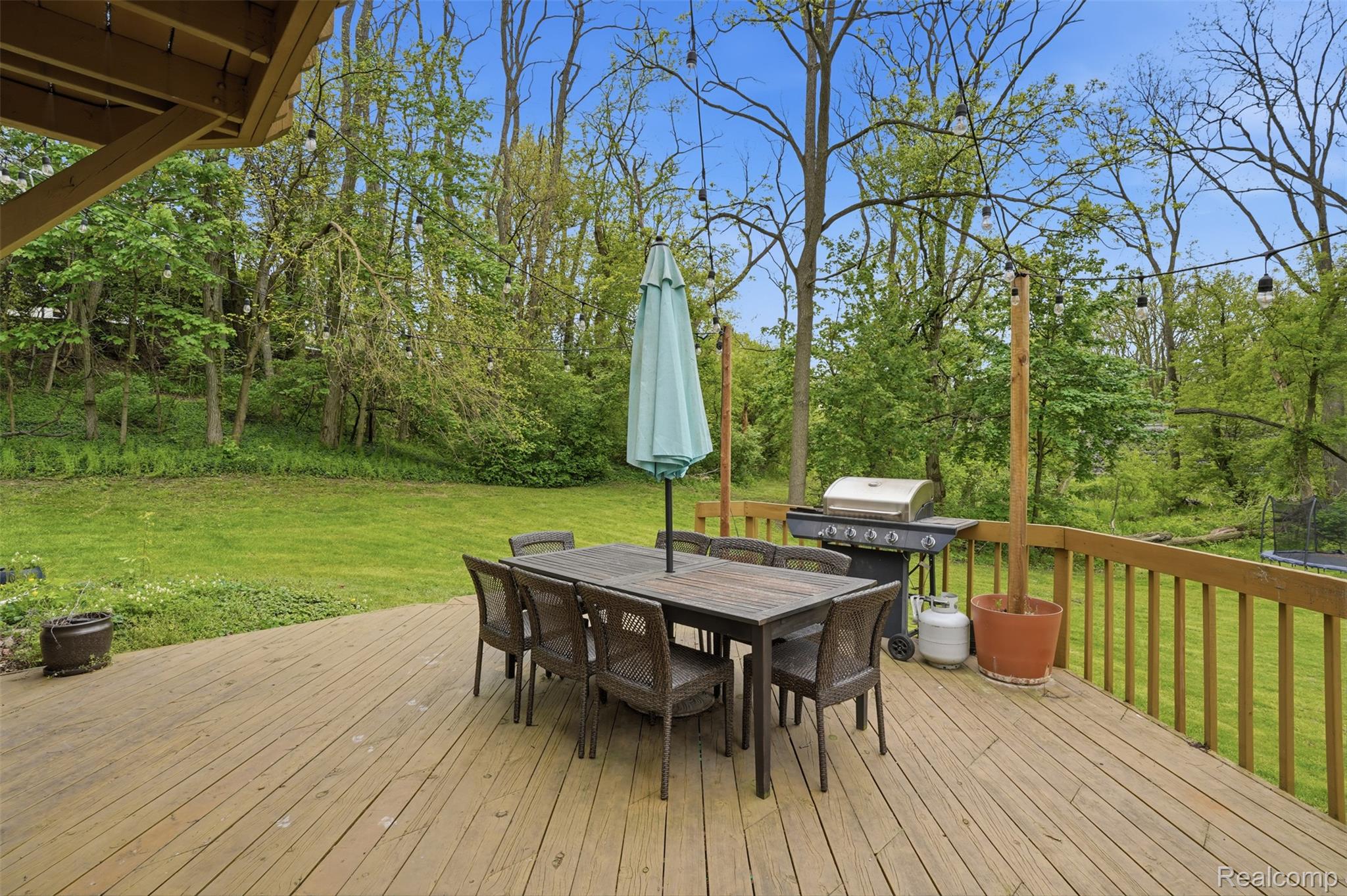47129 Dunsany Road Northville, MI 48167 - Photo 37 of 49 Wooden deck featuring a yard, outdoor dining area, a trampoline, and grilling area