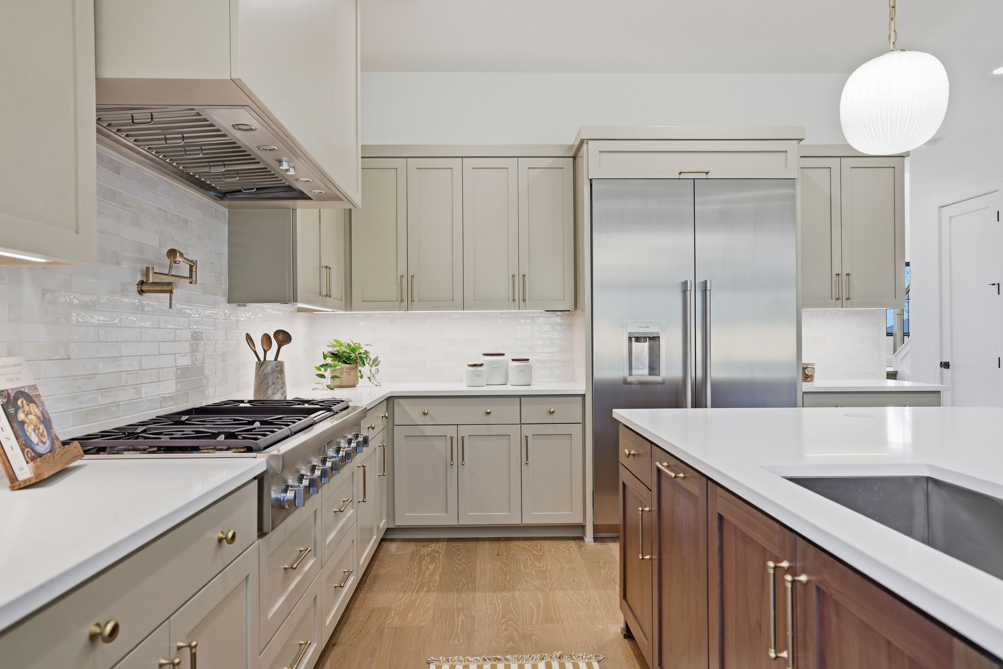 4500 Jinx Avenue Austin, TX 78745 - Photo 10 of 40 Two tone kitchen with dual tone cabinetry, stainless steel appliances, light wood-type flooring, light stone counters, and hanging light fixtures