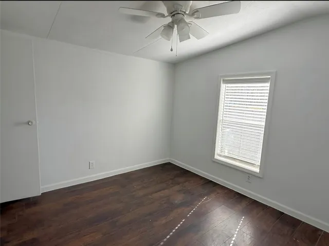 an empty room with wooden floor fan and windows