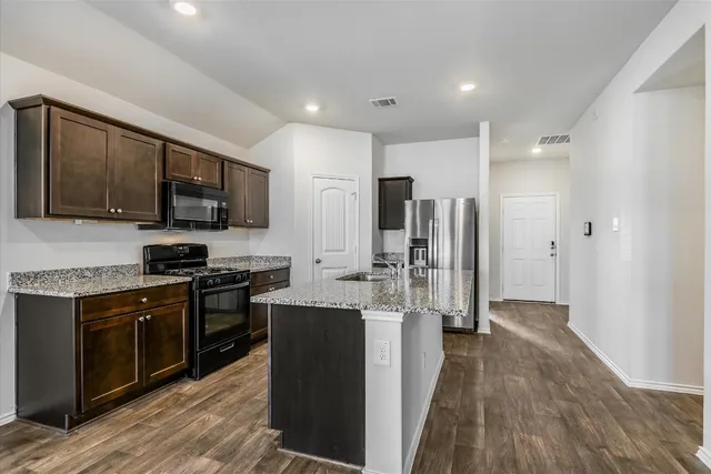 a kitchen with stainless steel appliances granite countertop a stove top oven a refrigerator a sink and dishwasher with wooden floor