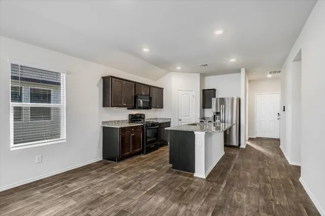 a kitchen with stainless steel appliances kitchen island granite countertop a stove top oven a sink dishwasher a refrigerator and a refrigerator with wooden floor