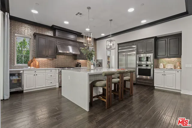 a kitchen with stainless steel appliances kitchen island granite countertop a stove a sink a refrigerator and white cabinets with wooden floor