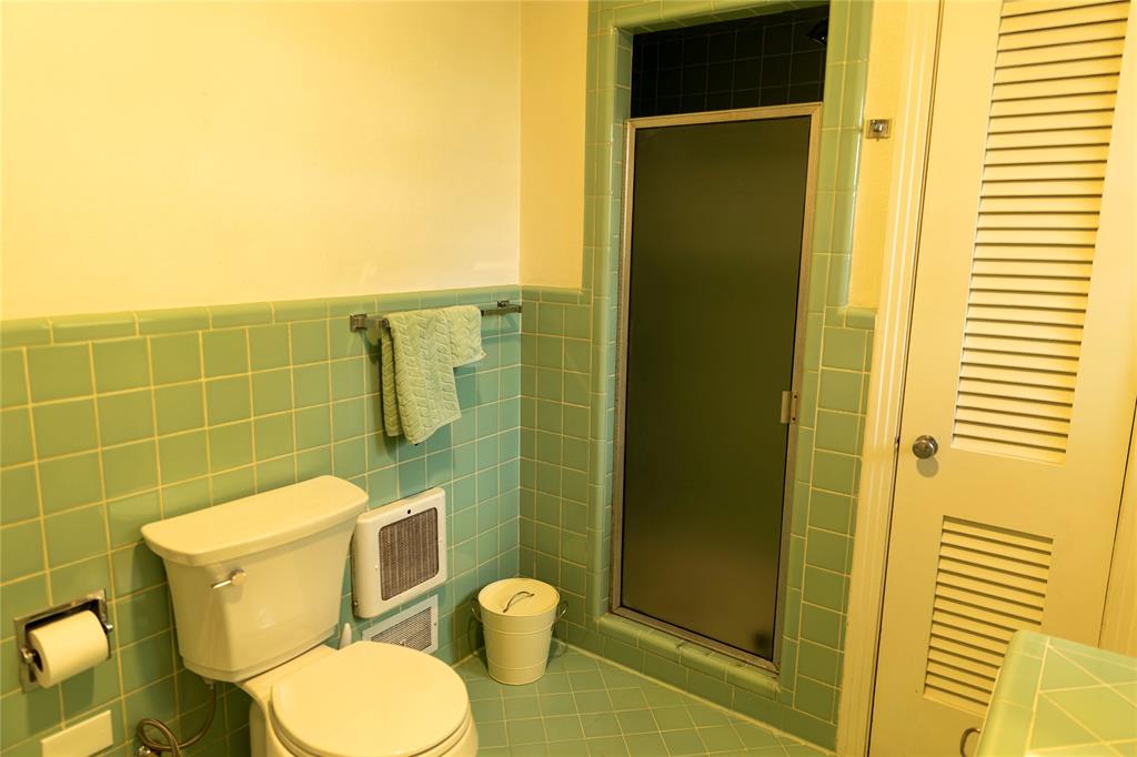 3228 Colcord Avenue Waco, TX 76707 - Photo 21 of 29 Bathroom with square green wall and floor tiling, a white toilet, and a stand-up shower with a frosted glass door
