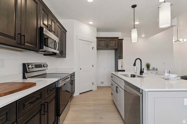 5777 West 4100 South Hooper, UT 84315 - Photo 10 of 41 Kitchen with stainless steel appliances, light wood-type flooring, an island with sink, dark wood finish cabinets, and light stone countertops