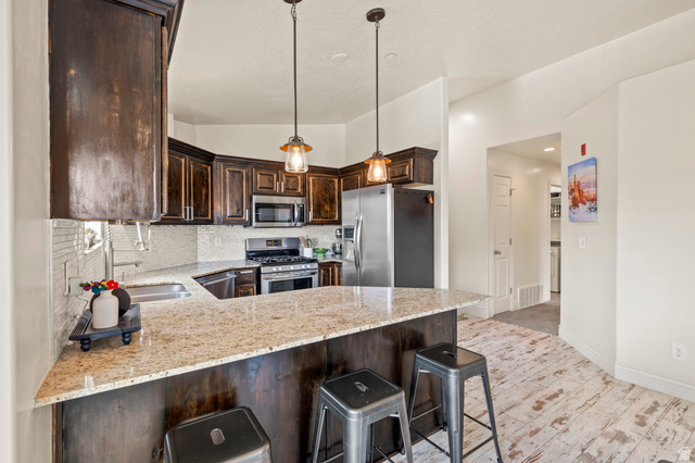 8248 South Resaca Drive, Unit J10 Sandy, UT 84070 - Photo 6 of 40 Kitchen featuring dark wood cabinetry, light-toned granite countertops, stainless steel appliances, a tile backsplash, and light wood-finish flooring