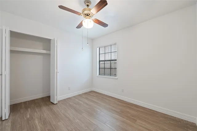 an empty room with wooden floor fan and windows