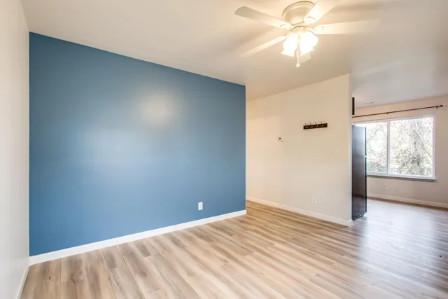 an empty room with wooden floor fan and windows