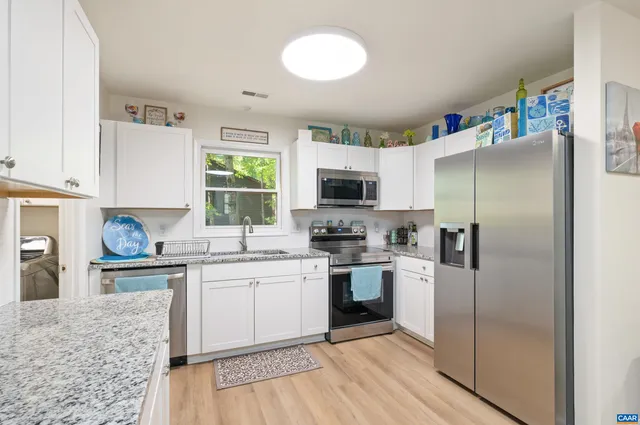 a kitchen with stainless steel appliances granite countertop white cabinets a sink a stove a microwave and wooden floors