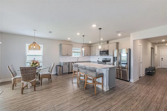 a kitchen with stainless steel appliances kitchen island granite countertop a table chairs refrigerator and sink