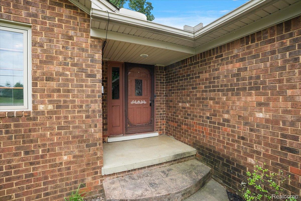 Brick exterior featuring a covered entry, transom window, patterned glass door, and concrete steps