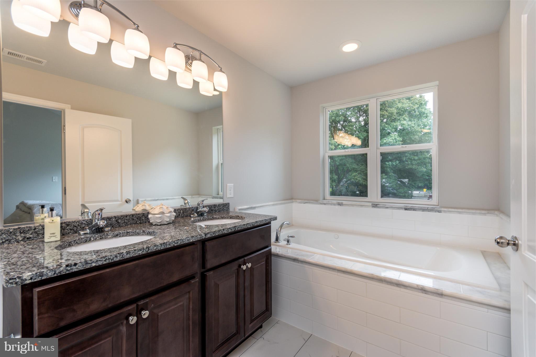 8035 Clark Station Road Severn, MD 21144 - Photo 15 of 24 a bathroom with a granite countertop bathtub a double vanity sink and a large mirror