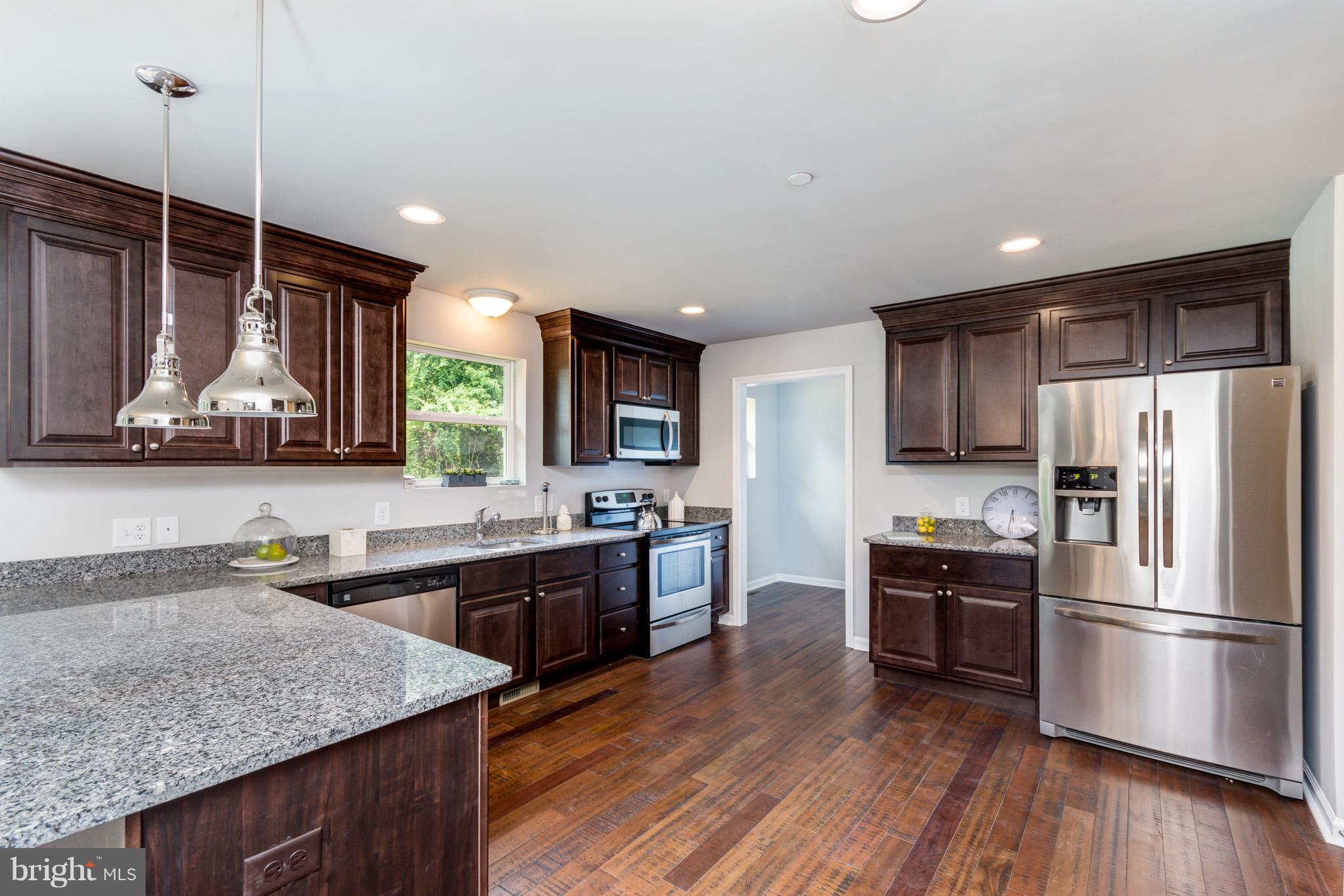8035 Clark Station Road Severn, MD 21144 - Photo 7 of 24 a kitchen with stainless steel appliances granite countertop a refrigerator a sink dishwasher a stove and white countertops with wooden floor