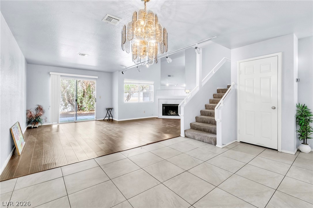 6250 West Flamingo Road, Unit 98 Las Vegas, NV 89103 - Photo 6 of 40 Unfurnished living room featuring stairs, a chandelier, light tile patterned flooring, visible vents, and a fireplace