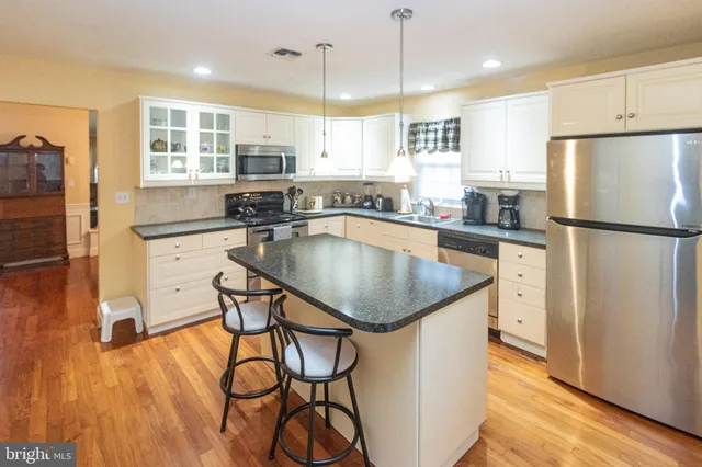 a kitchen with stainless steel appliances granite countertop a refrigerator a sink a stove and white cabinets with wooden floor