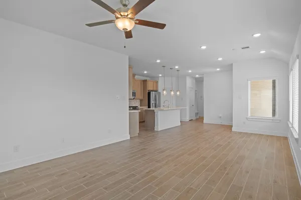 a view of an empty room with wooden floor and a ceiling fan