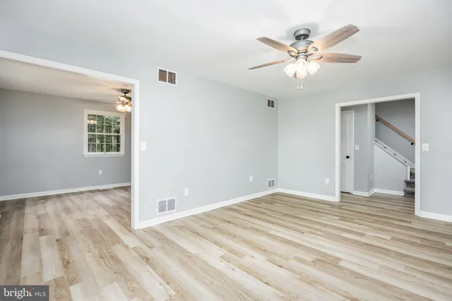 a view of an empty room with wooden floor and a chandelier fan