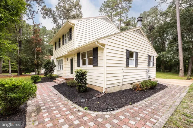 a view of a white house with a yard plants and large tree