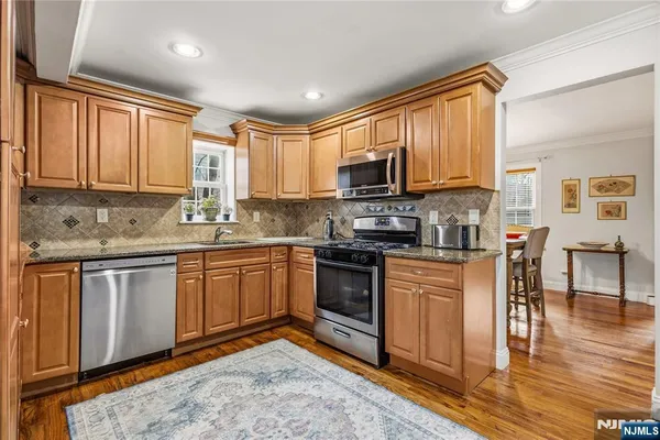 a kitchen with stainless steel appliances granite countertop a stove top oven a sink dishwasher a refrigerator and cabinets with wooden floor