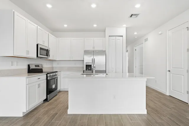 a large kitchen with stainless steel appliances granite countertop a stove a sink a refrigerator and white cabinets with wooden floor