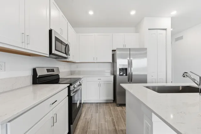 a kitchen with a sink dishwasher a refrigerator and white cabinets with wooden floor