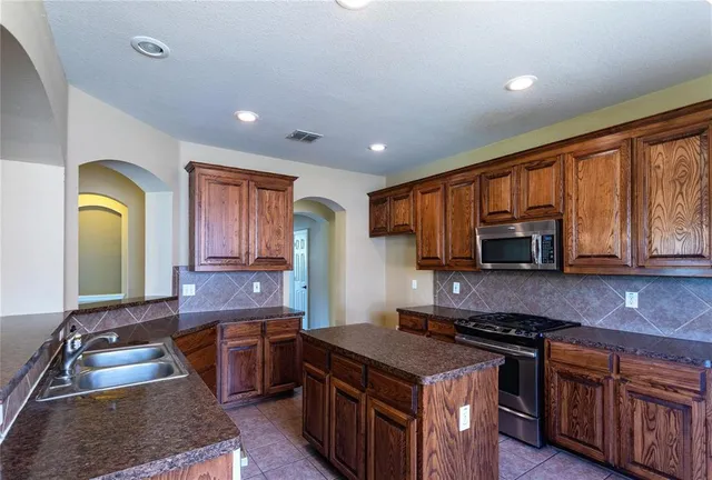 a kitchen with stainless steel appliances granite countertop a stove a sink dishwasher and a microwave oven with wooden cabinets