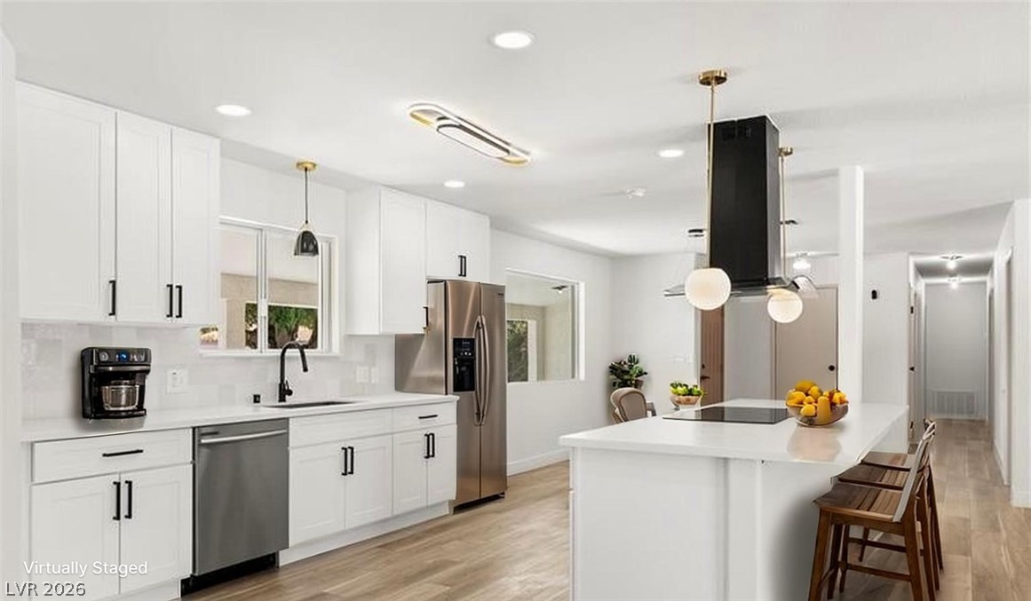Kitchen featuring island range hood, light wood-style flooring, white cabinetry, a kitchen bar, and stainless steel appliances Fridge no included