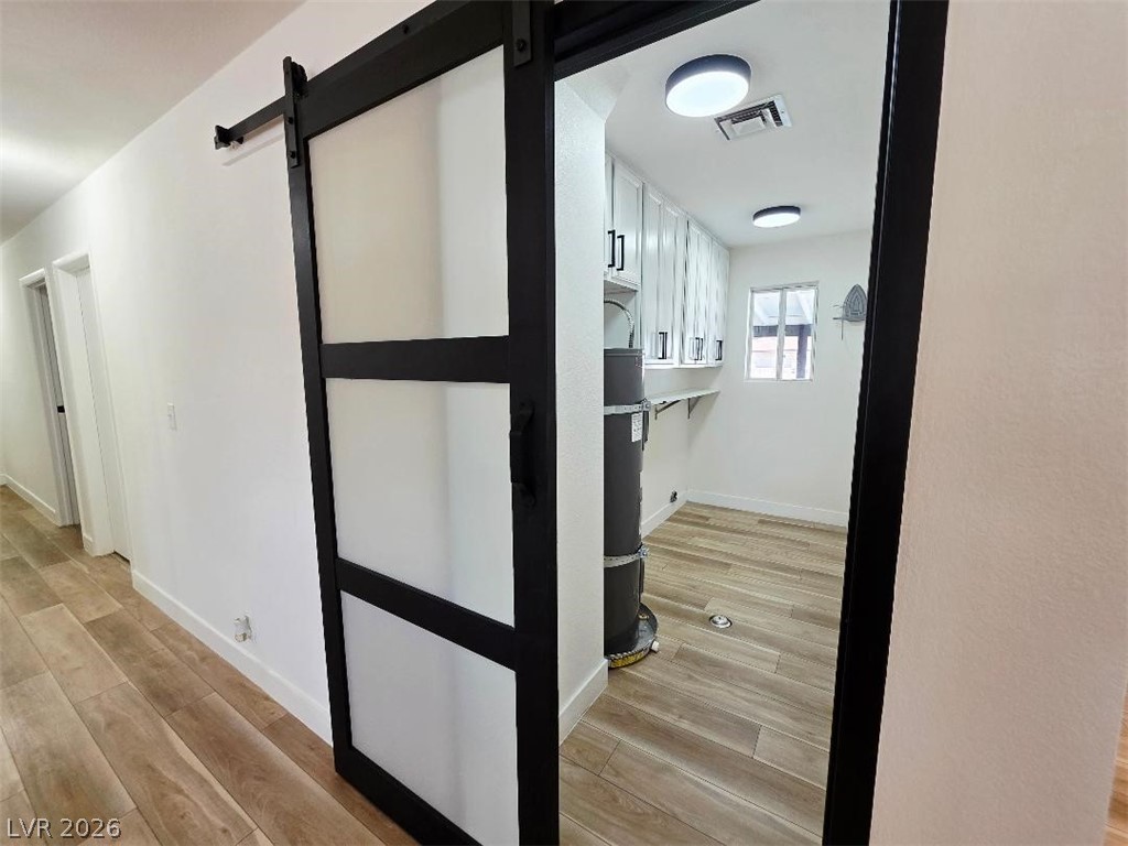 3420 West Warm Springs Road Las Vegas, NV 89118 - Photo 23 of 50 New deco barn door, light wood-style flooring, and New water heater, washer dryer room with white cabinets