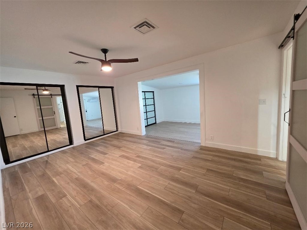 3420 West Warm Springs Road Las Vegas, NV 89118 - Photo 25 of 50 Primary Bedroom featuring multiple closets, light wood-style floors, and ceiling fan, barn door leading to primary bathroom with all black fixtures , with extra sitting area or 4th bedroom or office has large closets