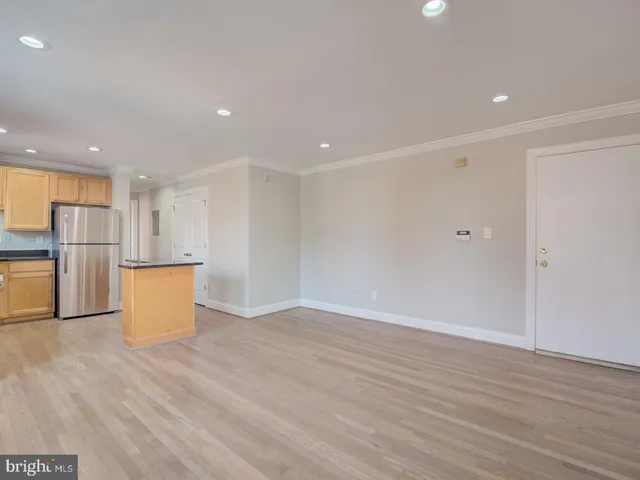 an empty room with wooden floor and kitchen view